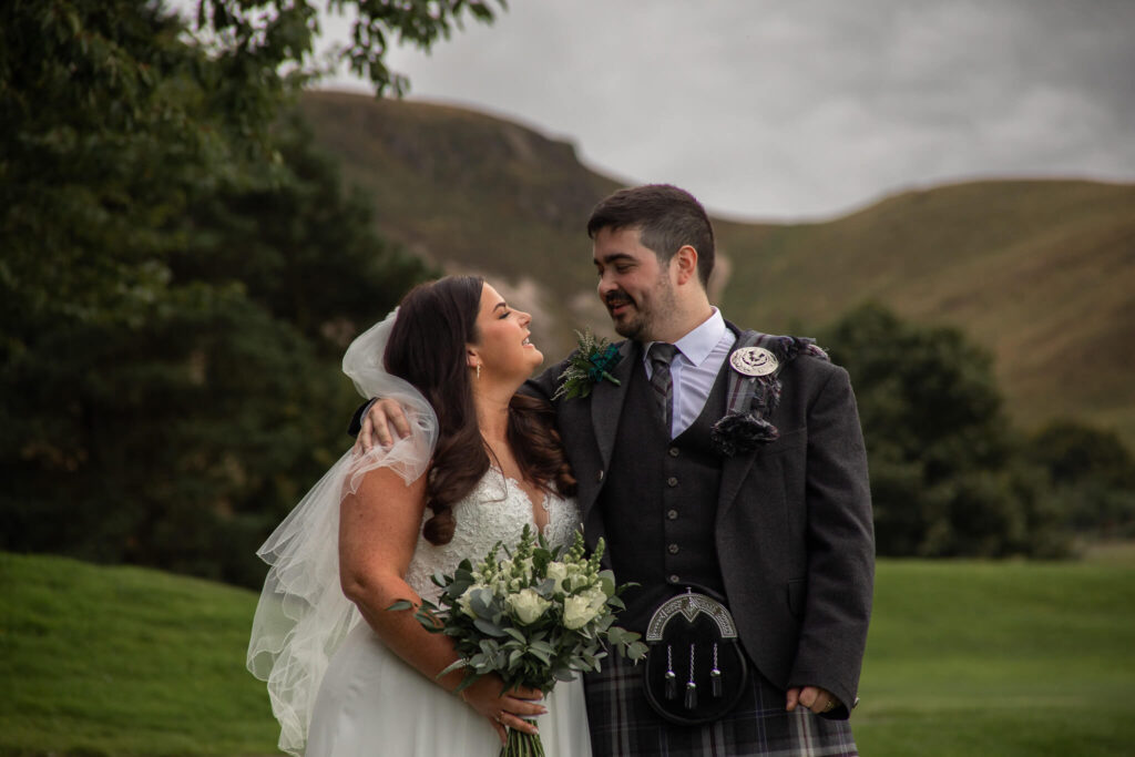 A photo of a newly married couples with hilly Scottish scenery behind them